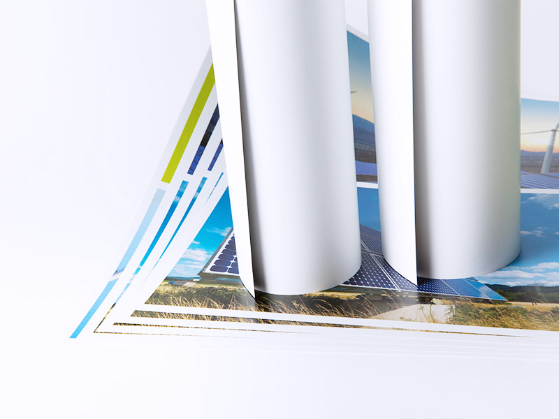 Zwei aufgerollte Plakate nebeneinander, die auf einem Fächer von Plakaten stehen, de ein ländliches Motiv mit blauem Himmel zeigen. Die Rollen sind mit der weißen Außenseite sichtbar.